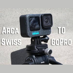 May include: A black GoPro camera mounted on a black tripod. The camera has a screen and a lens. The text "ARCA SWISS TO GOPRO" is displayed in white. The GoPro logo is visible in blue.