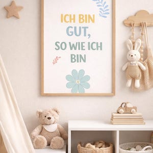 Könnte beinhalten: Ein gerahmter Druck mit dem deutschen Text "ICH BIN GUT, SO WIE ICH BIN" in Gelb, Blau und Grün, mit floralen Akzenten. Der Raum zeigt einen Stern, einen Teddybären und ein Spielzeugauto.