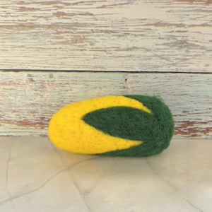 May include: A handmade felted object in a rounded shape, featuring a vibrant yellow and green color scheme. The design incorporates a curved, leaf-like pattern in green against a yellow backdrop. The object is likely a decorative item.