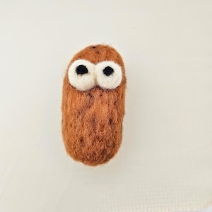 May include: A handmade, brown felted creature with large, white-rimmed eyes and black pupils. The whimsical design resembles a stylized owl or cartoon character, perfect for a child's room or as a unique decorative item.