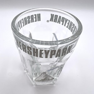 May include: Clear glass shot glass with the text "Hersheypark" printed in gold around the rim and a Hershey's Kisses logo on the bottom.