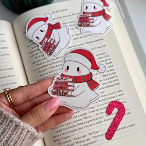 May include: White ghost stickers wearing Santa hats and scarves, holding stacks of books. A red glitter candy cane and a book are also in the image. The stickers have the text "BonitaCraftyShop".