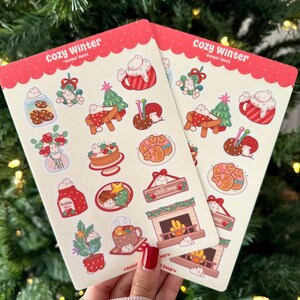 May include: Two sticker sheets with a red border and the text "Cozy Winter". The stickers feature winter-themed illustrations, including cookies, hot cocoa, a fireplace, and a Christmas tree. The stickers are in a cute, cartoon style.