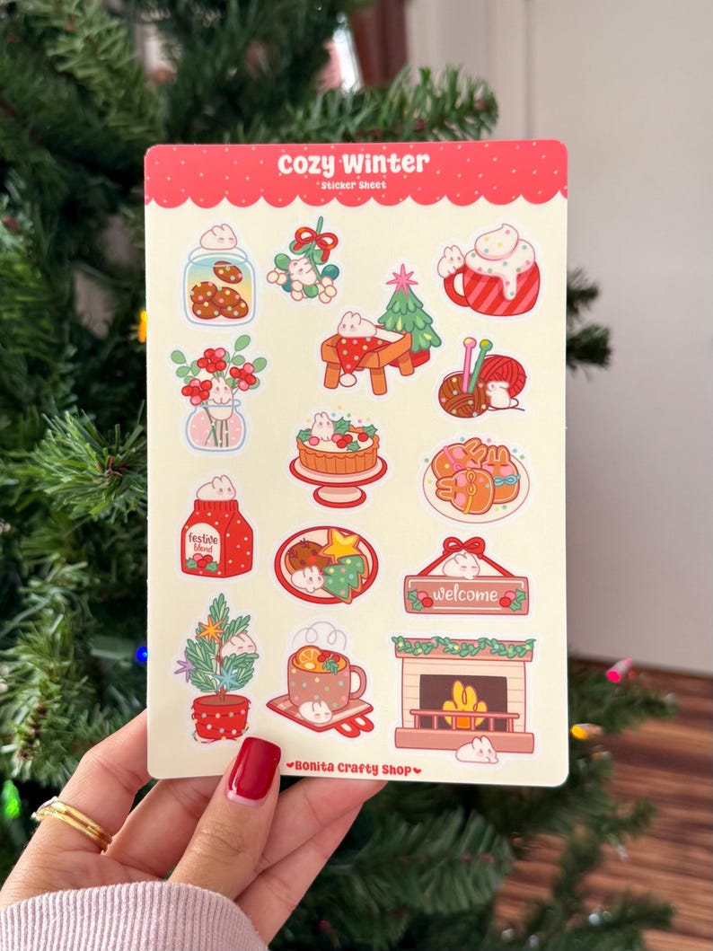 May include: A sticker sheet with a red border and the words "cozy Winter" at the top. The sheet features various winter-themed illustrations, including cookies, a Christmas tree, a mug of hot cocoa, and a fireplace. The bottom right corner has the text "Bonita Crafty Shop".