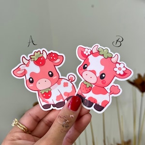 May include: Two die-cut stickers labeled A and B, each featuring a cartoon cow with pink and white patches. Sticker A shows a cow with a strawberry on its head. Sticker B shows a cow with white flowers on its head and a strawberry near its chin.