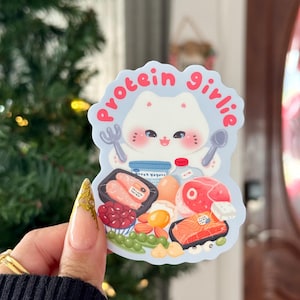 Może przedstawiać: Naklejka z kresk&oacute;wkowym kotem trzymającym widelec i łyżkę, otoczonym ilustracjami bogatych w białko produkt&oacute;w spożywczych. Tekst "protein girlie" jest napisany w okrąg wok&oacute;ł głowy kota. Naklejka jest jasnoniebieska i biała.