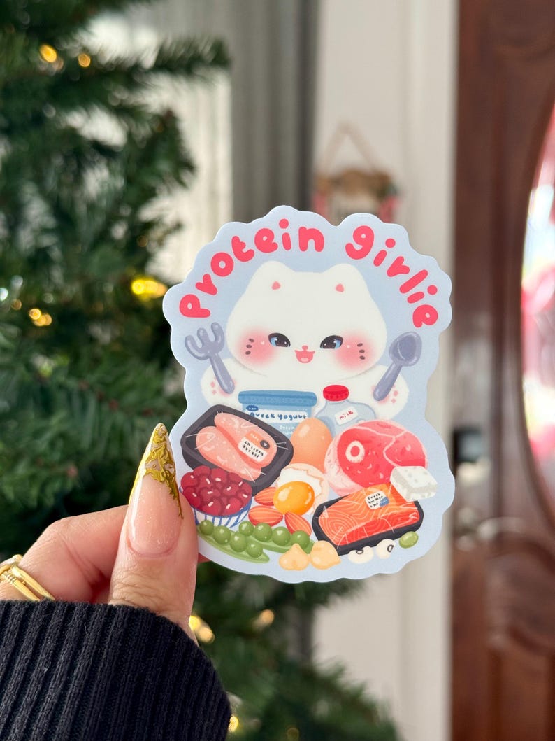 Może przedstawiać: Naklejka z kresk&oacute;wkowym kotem trzymającym widelec i łyżkę, otoczonym ilustracjami bogatych w białko produkt&oacute;w spożywczych. Tekst "protein girlie" jest napisany w okrąg wok&oacute;ł głowy kota. Naklejka jest jasnoniebieska i biała.
