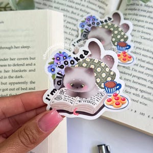 May include: A sticker featuring a cartoon cat with the text "I'm all booked." The cat is depicted with a book, a cup of coffee, and cookies. The sticker has a floral and patterned design.