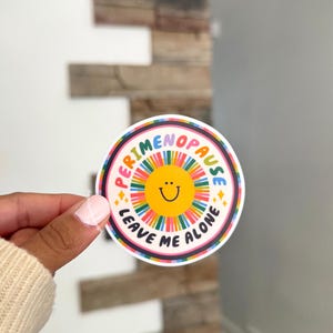 Pu&ograve; includere: Un adesivo circolare con una faccina sorridente gialla al centro circondata da un motivo a raggiera colorato. Il testo PERIMENOPAUSE LEAVE ME ALONE &egrave; stampato in lettere maiuscole nere lungo il bordo, accentuato da piccole stelle gialle.