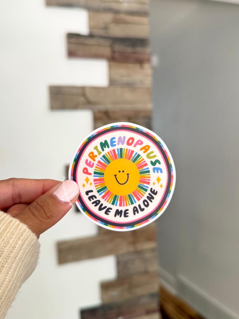 Pu&ograve; includere: Un adesivo circolare con una faccina sorridente gialla al centro circondata da un motivo a raggiera colorato. Il testo PERIMENOPAUSE LEAVE ME ALONE &egrave; stampato in lettere maiuscole nere lungo il bordo, accentuato da piccole stelle gialle.