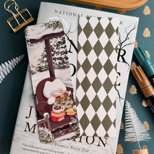 May include: A stack of books with two decorative bookmarks and a gold binder clip. One bookmark features a cartoon character reading in a snowy scene. The other has a green and white diamond pattern. The book is titled "Promise Not to Tell."