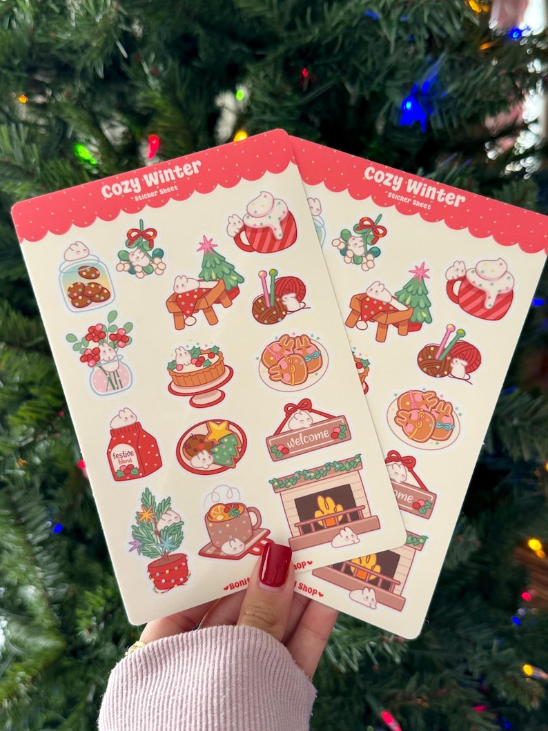 May include: Two sticker sheets with a red scalloped border and the text "Cozy Winter." Each sheet features winter-themed illustrations, including gingerbread cookies, a fireplace, and a mug of hot cocoa. The text "Festive Mind" and "Welcome" are also visible.