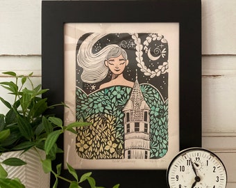 May include: A framed black and white print of a woman with long hair, a tower, and a crescent moon. The print is surrounded by a green and yellow floral design. The text "Wild Dreaming" and "Forever Wild" is visible at the bottom of the print.