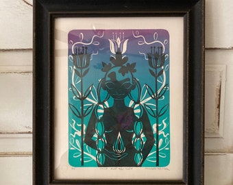 May include: A framed print of a woman with a crown of flowers, standing in a garden with stylized flowers and leaves. The print is in shades of blue, green, and purple. The text "cant will the tide" and "purple willow" is visible at the bottom of the print.