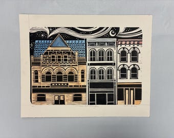 May include: A block print illustration on cream paper depicting three multi-story buildings under a night sky with stars and a crescent moon. The buildings feature arched windows, a blue roof, and tan facades, rendered in black, blue, and tan ink.