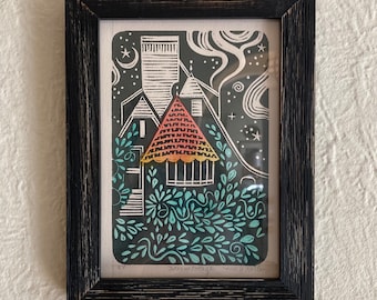 May include: A black framed print of a colorful illustration of a house with a red roof and green foliage. The text "Dream Cottage" and "Nicole Heller" is printed below the image.