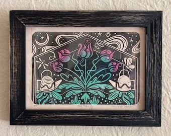 May include: Framed art print with a black distressed frame. The print features a stylized floral design in teal, purple, and white against a black background. The words "Tea Party" are visible. The artwork includes teapots, flowers, and celestial elements.