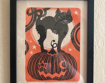 May include: Framed art print featuring a black cat standing on a carved pumpkin. The print has an orange background with white stars and swirls. The words "Black cat" are printed at the bottom.