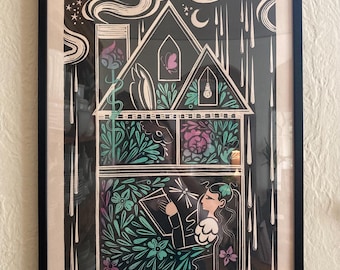 May include: A black and white linocut print of a house with a woman reading a book inside. The house is filled with plants and flowers, and the woman is surrounded by a glowing light. The print is framed in black.