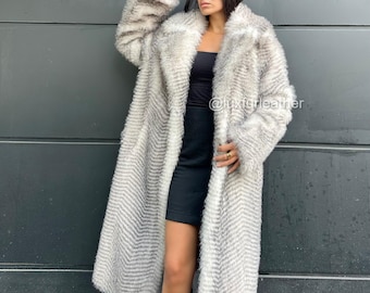 May include: A long, faux fur coat in shades of gray and white, featuring a chevron pattern. The coat has a wide collar and a full length design. The text "@luxuryleather" is visible on the image.