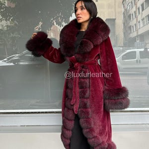 May include: A long, burgundy faux fur coat with a large collar and cuffs. The coat features a matching belt and is trimmed with darker fur accents. The text "@luxfurleather" is visible on the coat.