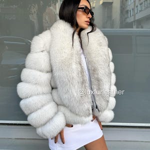 Puede incluir: Chaqueta de piel blanca con cremallera y cuello ancho. La chaqueta presenta un diseño en capas en las mangas y el cuerpo. El texto "@luxfurleather" es visible en la chaqueta.