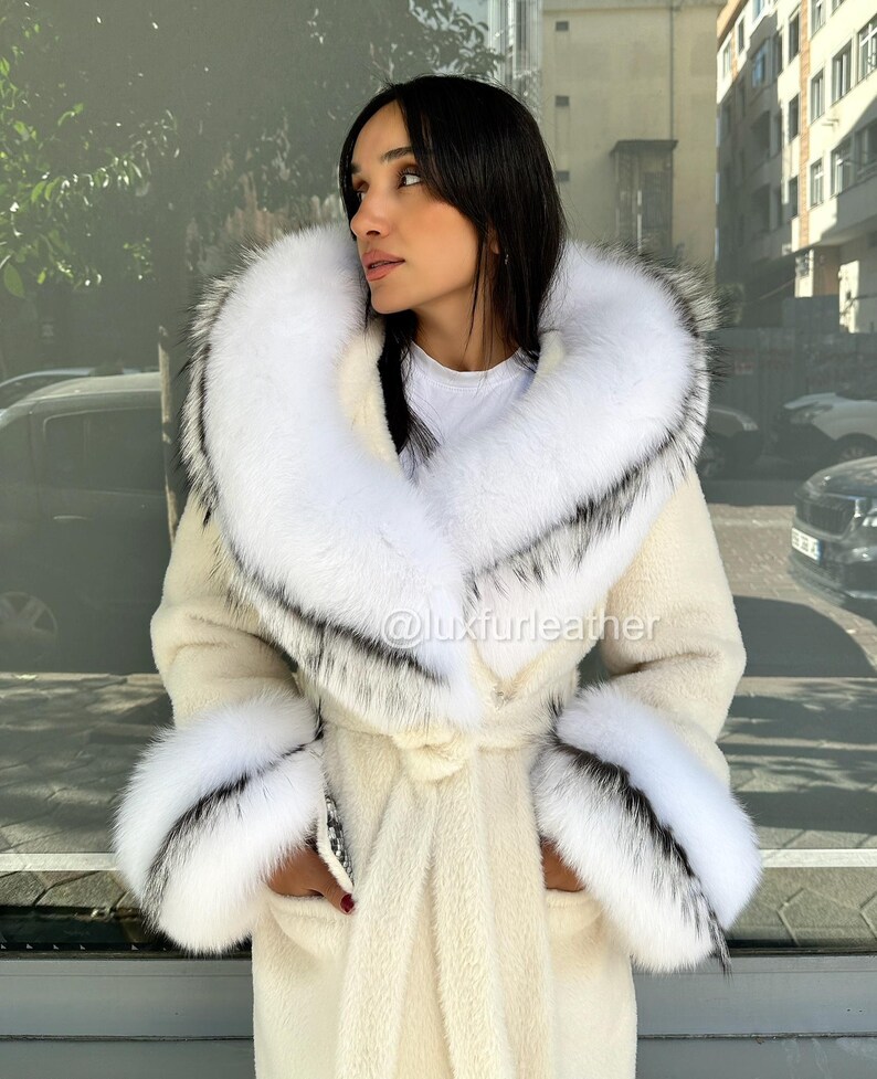 May include: Cream-colored coat with a large white fur collar and cuffs, accented with black and gray details. The coat features a belted waist and is worn by a person. The Instagram handle @luxfurleather is visible.