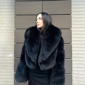 May include: A black fur coat with a large, dramatic collar. The coat is cropped at the waist and has long sleeves.