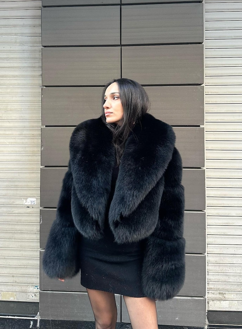 May include: A black fur coat with a large, dramatic collar. The coat is cropped at the waist and has long sleeves.