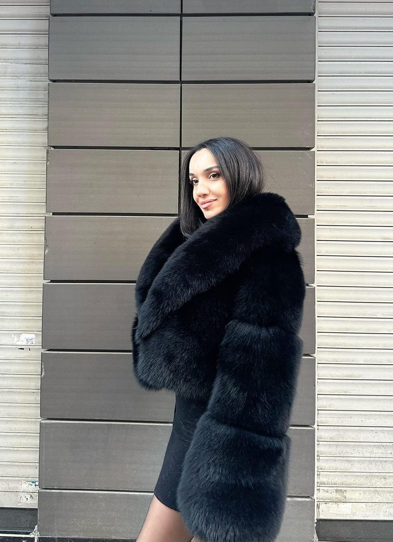 May include: A black faux fur jacket with a large collar and long sleeves. The jacket is cropped at the waist and has a fitted silhouette.