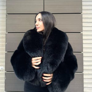 May include: A black fur jacket with a large collar. The jacket is cropped and has a fitted silhouette.