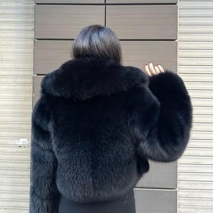 May include: A black faux fur jacket with a large collar. The jacket is cropped and has long sleeves.