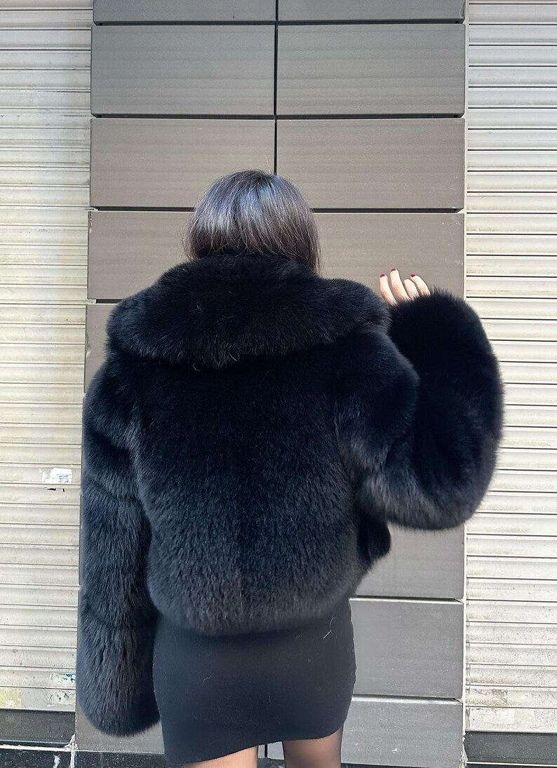 May include: A black faux fur jacket with a large collar. The jacket is cropped and has long sleeves.