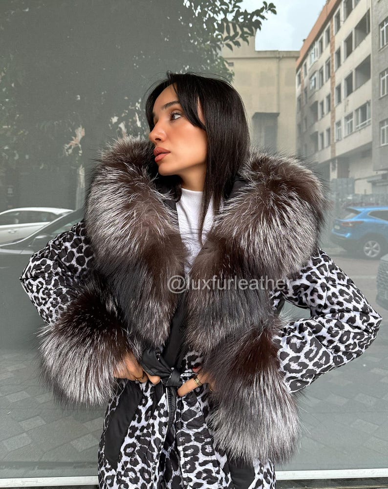 Op de afbeelding: Een zwart-witte jas met luipaardprint met een grote bontkraag en manchetten. De jas heeft een ceintuur in de taille. De tekst "@luxfurleather" is zichtbaar op de jas. Gedragen door een persoon.