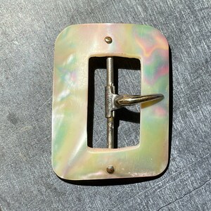 May include: A rectangular iridescent mother of pearl belt buckle with a silver metal buckle and a gold-toned metal prong.