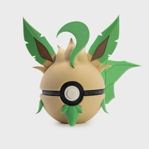 May include: A detailed, 3D-printed model of a Pokémon character. The figure is primarily tan with green and brown accents, featuring leaf-like structures and a black and white circular design. The overall shape is spherical with pointed details.