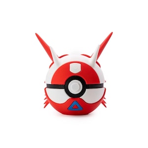 May include: A red, white, and black spherical collectible with two red horns and a blue triangle. The item has a button in the center and is a stylized version of a Poke Ball.