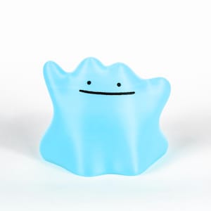 Pode incluir: Uma figura azul clara em forma de mancha com um rosto sorridente. A figura tem uma forma suave e arredondada e uma simples linha preta para a boca e dois pontos para os olhos. O fundo é branco liso.