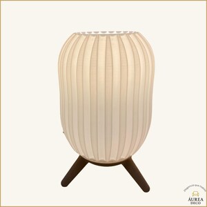 May include: A cream-coloured, ribbed table lamp with a rounded, vase-like shade. The lamp sits on three dark brown, angled legs. The lamp's shade has vertical lines. The lamp is a decorative lighting fixture.