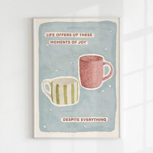 May include: Framed art print with two mugs on a blue backdrop. One is pink, the other white with green stripes. Text reads "LIFE OFFERS UP THESE MOMENTS OF JOY DESPITE EVERYTHING."