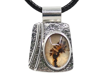 May include: A silver pendant necklace with a rectangular, textured frame. The pendant features an oval-shaped stone with a brown and beige dendritic pattern. The necklace has a black cord.