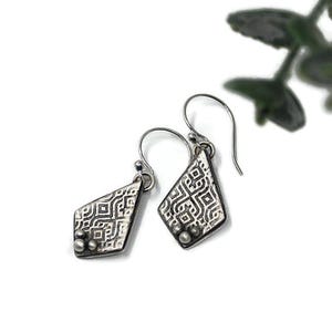 May include: A pair of silver earrings with a geometric pattern and three small silver beads on each earring.