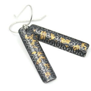 May include: A pair of silver dangle earrings with a black and gold patterned design. The earrings are rectangular in shape and have a floral pattern.