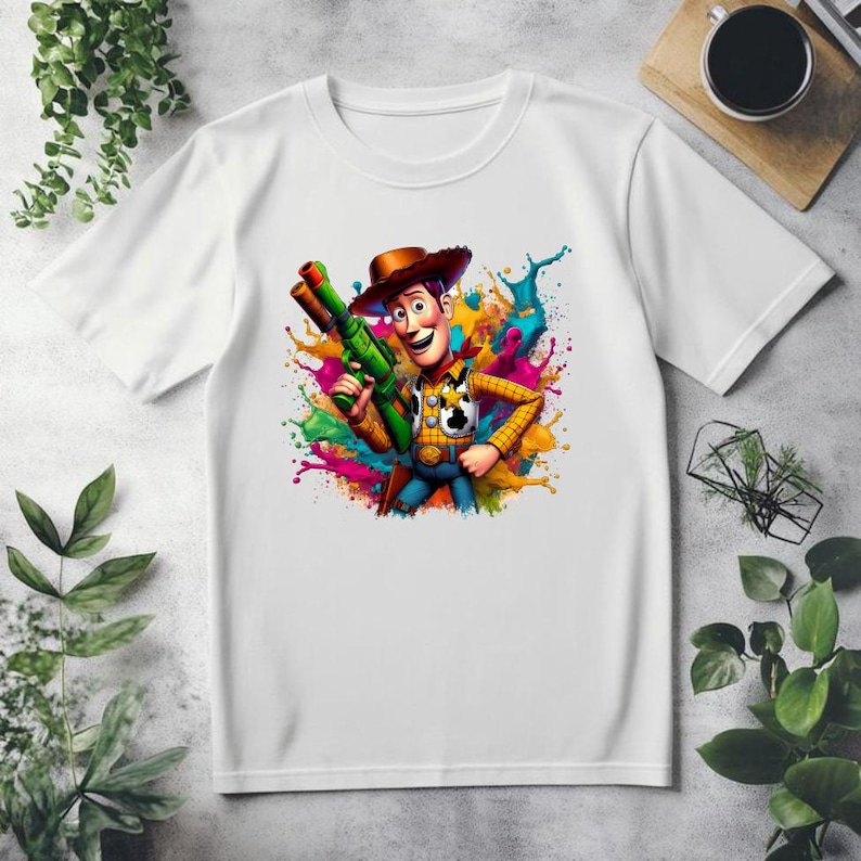 May include: White t-shirt with a colorful paint splatter design featuring Woody from Toy Story holding a green toy gun.