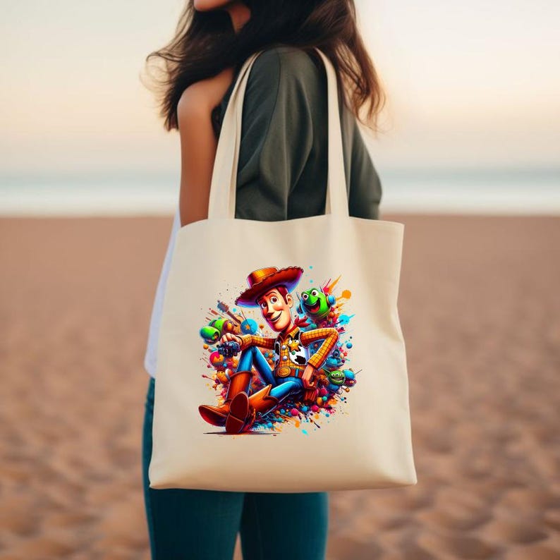 May include: A white canvas tote bag with a colorful graphic print of Woody from Toy Story. Woody is sitting with his legs crossed and holding a gun. He is surrounded by colorful paint splatters.