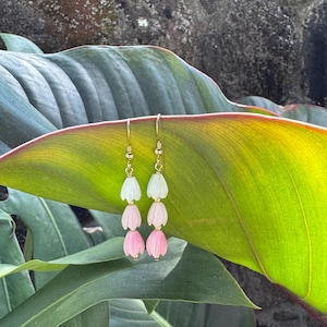 May include: A pair of gold dangle earrings with three pink and white flower-shaped beads on each earring.