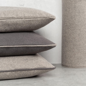 Puede incluir: Tres almohadas decorativas apiladas una encima de la otra. La almohada superior es de color gris claro, la almohada del medio es de color gris oscuro y la almohada inferior es de color gris claro. Las tres almohadas tienen un ribete contrastante alrededor de los bordes.