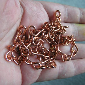 Puede incluir: Primer plano de una cadena de cobre con un diseño de bucle. La cadena está en una mano, pero la mano no es visible en la imagen.