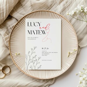 Pode incluir: Um convite de casamento em um prato creme. O convite é branco com texto preto e vermelho que diz "LUCY and MATEW" e "INVITE YOU TO SHARE IN THEIR WEDDING DAY". A data é 25 de outubro de 2026.