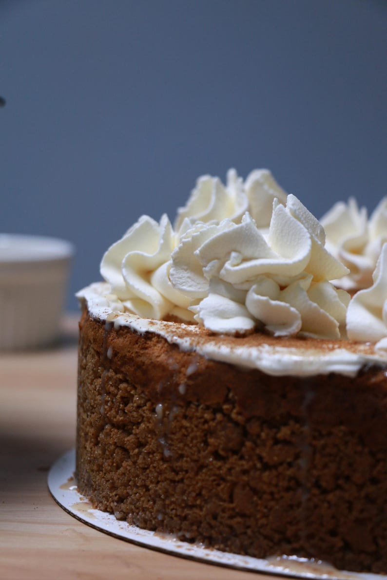 K&ouml;nnte beinhalten: Nahaufnahme eines runden Kuchens mit brauner Kruste und einer Schicht wei&szlig;er Schlagsahne obenauf. Der Kuchen befindet sich auf einer wei&szlig;en Papierunterlage.